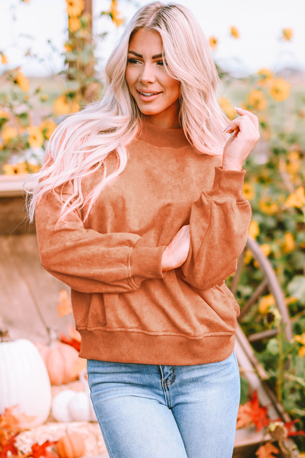 A person with long blonde hair wearing an Orange Drop Shoulder Crew Neck Pullover Sweatshirt and blue jeans stands with their back to the camera in a sunflower field.