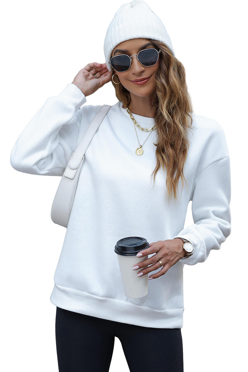 A person wearing a white beanie, the EVERY THING WILL BE OKAY Colorful Letters Sweatshirt, and sunglasses, holding a coffee cup, stands outside near windows.