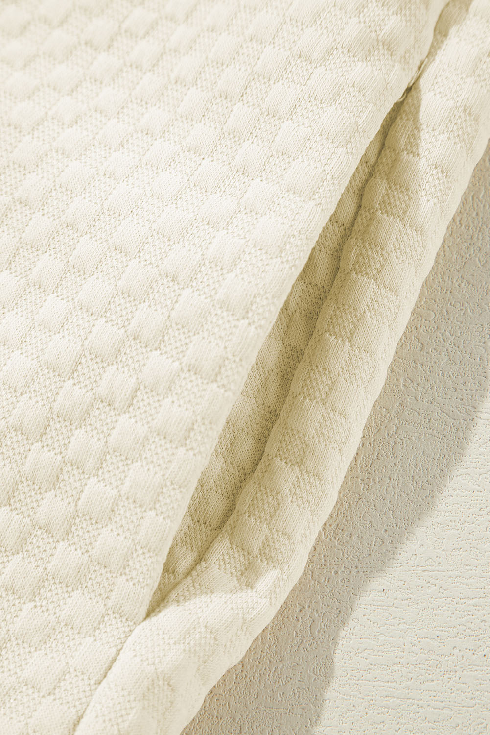 A person stands indoors facing away, wearing the Apricot Textured Buttoned Neckline Side Pockets Hoodie and black shorts. Their hand rests on their hip.