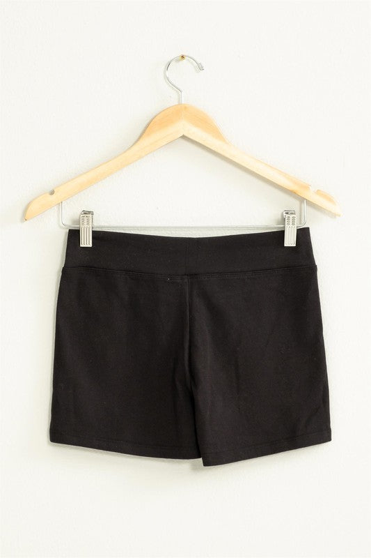 The Take Pride Mid-Rise Biker Shorts, crafted from stretch fabric, hang gracefully on a wooden hanger against a pale wall.