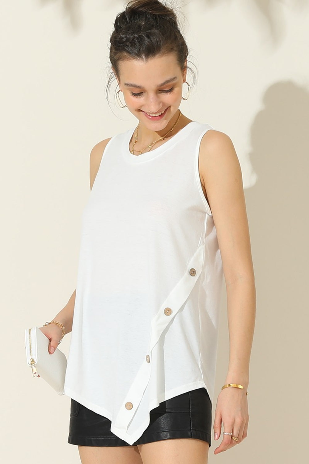 A woman wearing the Ninexis Round Neck Button Side Tank and white shorts stands against a light-colored background, smiling. She is accessorized with gold jewelry, showcasing her summer wardrobe.