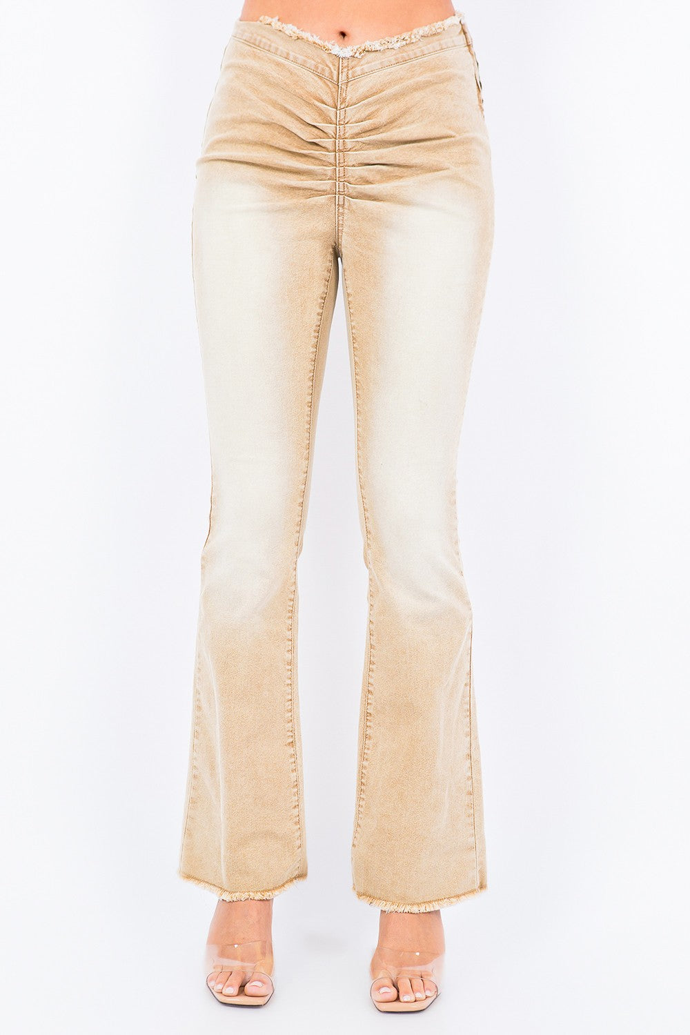 A person is wearing American Bazi V-Cut Ruched Flare Pants in light beige with frayed hems, paired with transparent high-heeled sandals.