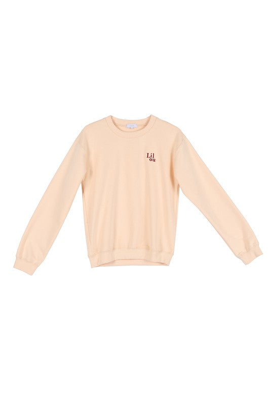 A person wearing a cream sweatshirt with embroidered "Lilou" logo is standing against a white background.