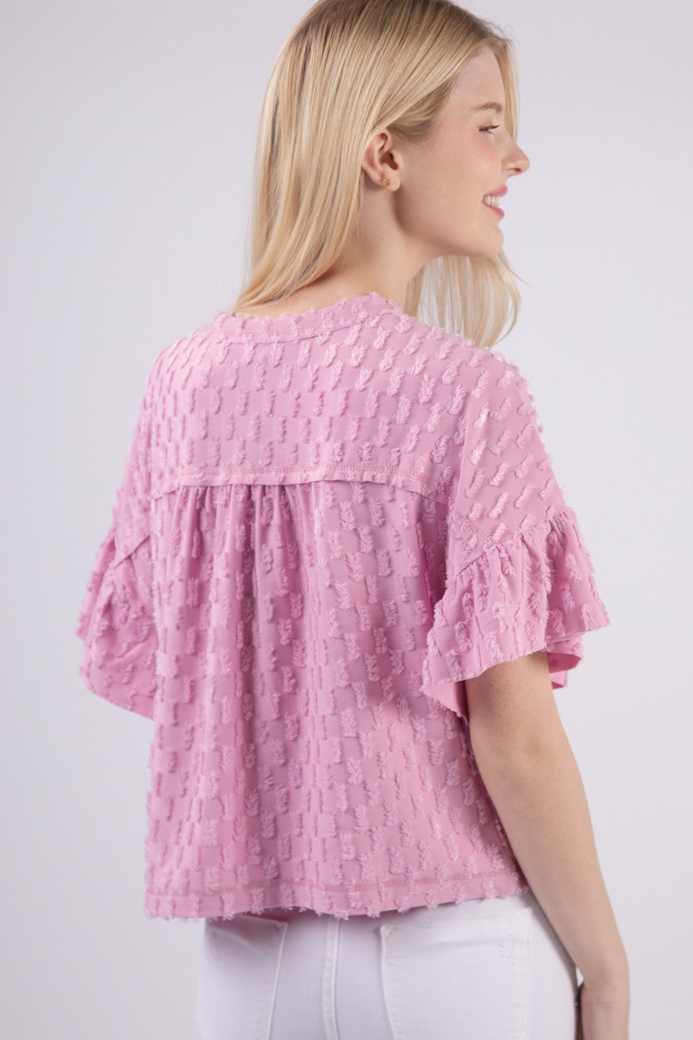 Person wearing the VERY J Full Size Texture Ruffle Short Sleeve Top, a chic and feminine textured pink blouse, paired with white pants, standing against a plain background.