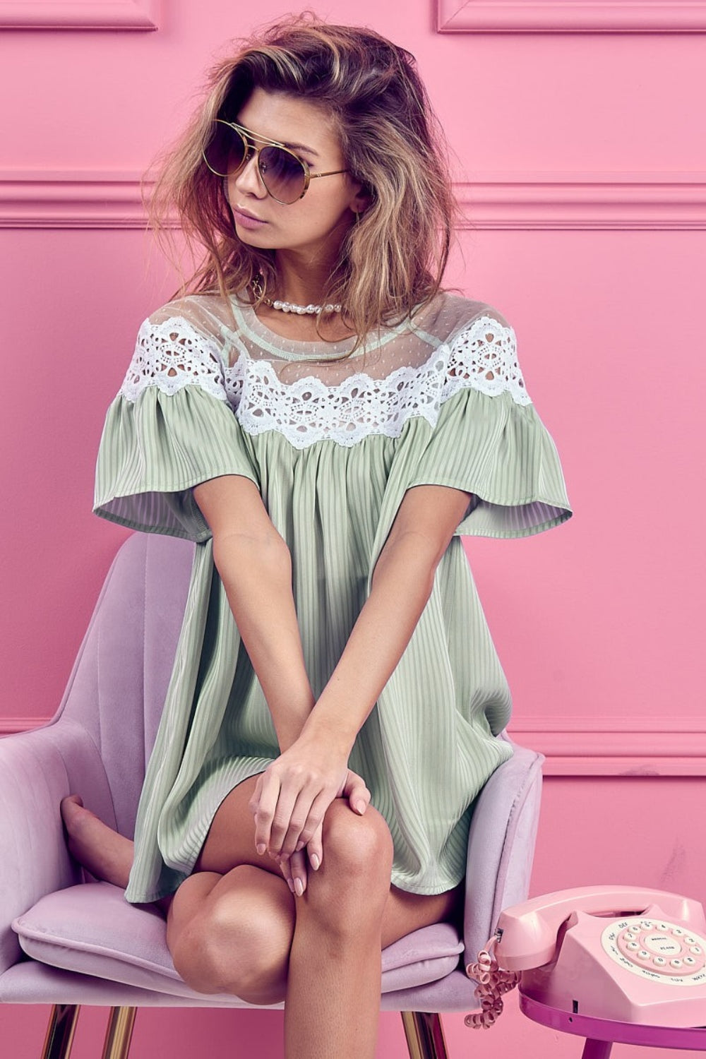 A woman wearing a BiBi Lace Detail Short Sleeve Striped Blouse and sunglasses poses against a pink background.