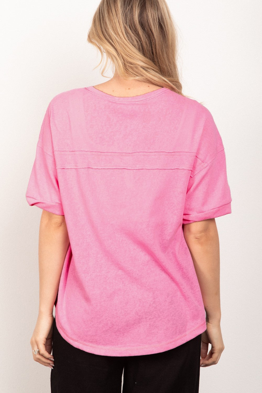 A person with long blonde hair is wearing the VERY J Twisted Sleeve Band Half Button Top in pink, standing in front of a plain white background.