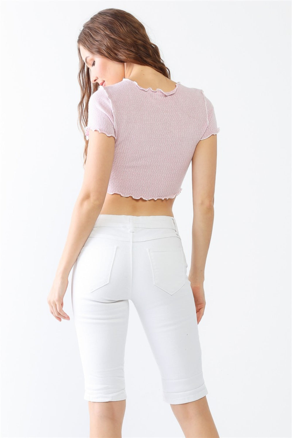 A woman in a lilac crop top and LITZ LA Distressed Bermuda Denim Shorts stands against a plain background, effortlessly channeling a vintage feel.