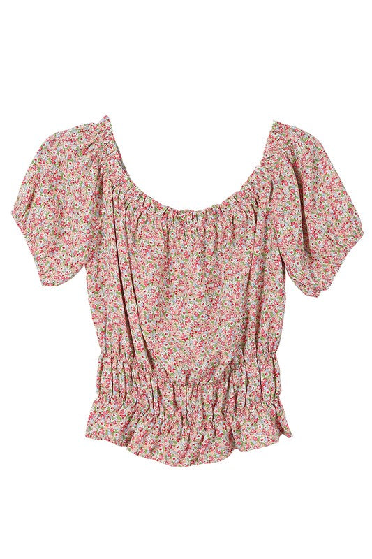 A woman wears the SL off shoulder tube top, featuring a floral print and a shirred design. The ensemble is completed with puffed sleeves and a ruffled skirt for an elegant and charming look.