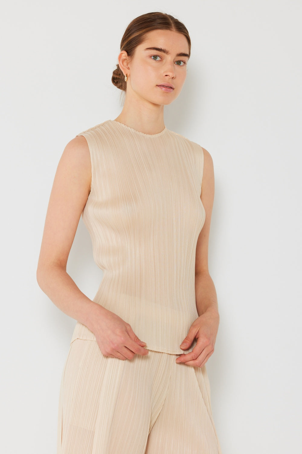 Person wearing a Marina West Swim Pleated Sleeveless Crewneck Tank and a gray pleated skirt, standing against a white background.