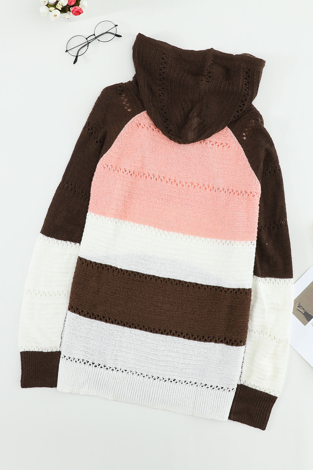 A person stands with their back to the camera, adjusting the hood of a Brown Beach Bonfire Knitted Hoodie featuring dark brown, pink, white, and light brown stripes. Perfect for a casual style, they are wearing distressed blue jeans and showcasing the laid-back vibe of lightweight hoodies.