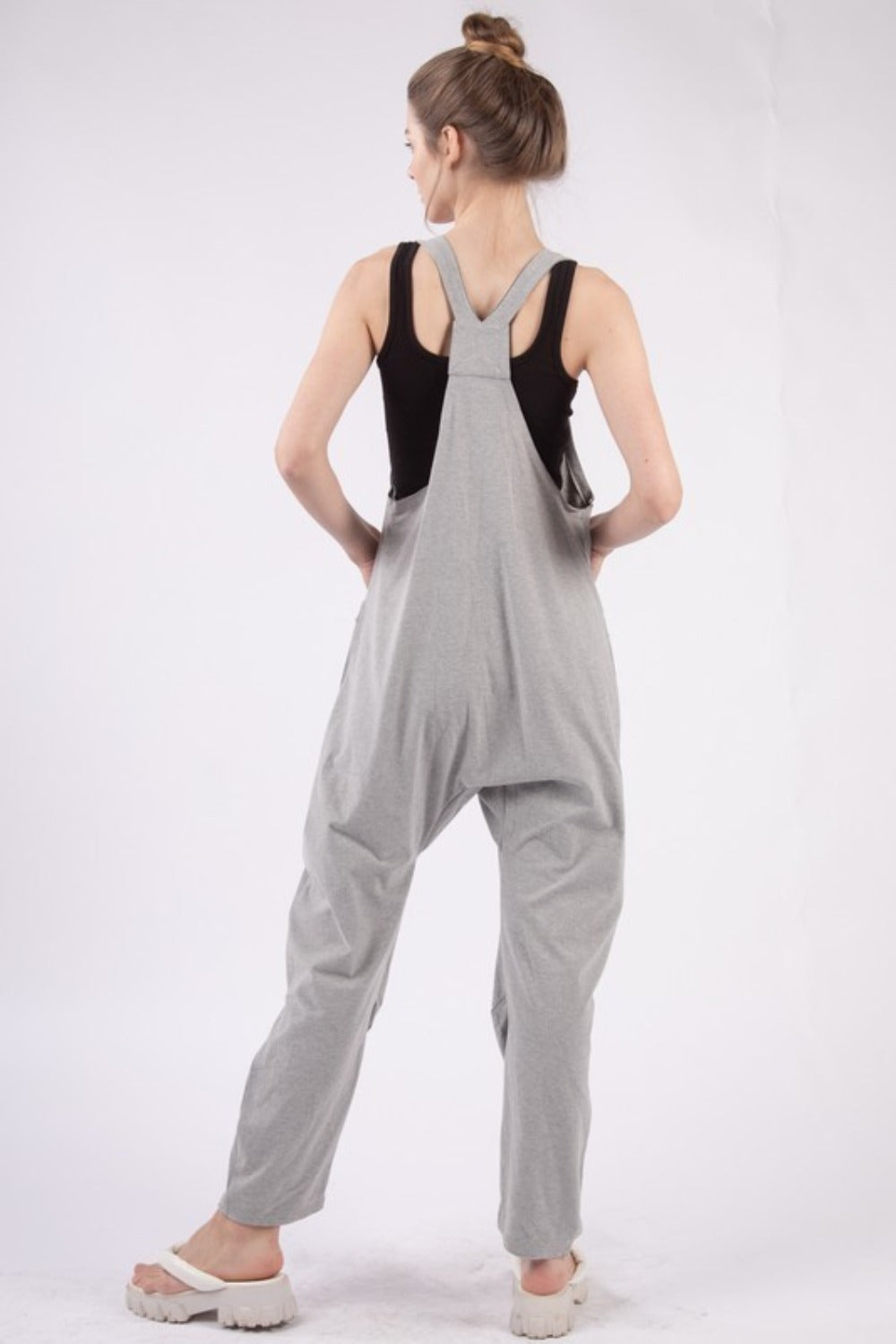 A person wearing the VERY J Plunge Sleeveless Jumpsuit with Pockets in gray and white sandals stands against a plain white background.