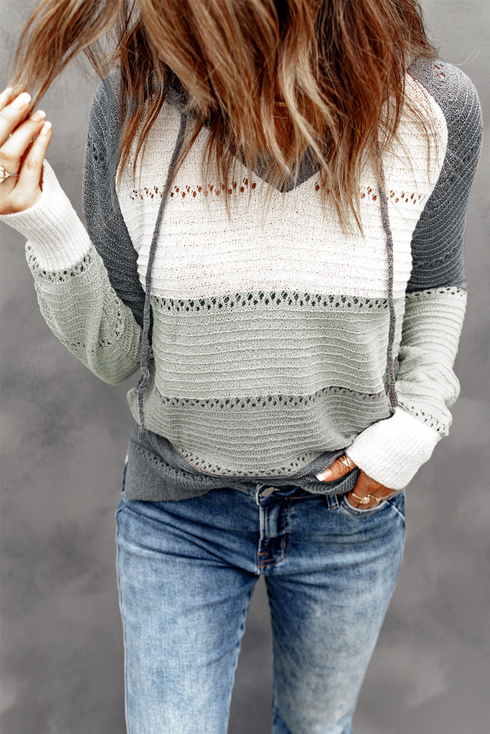 Rear view of a person with long hair wearing the Beach Bonfire Knitted Hoodie and blue jeans, showcasing one of our casual styles against a gray background.