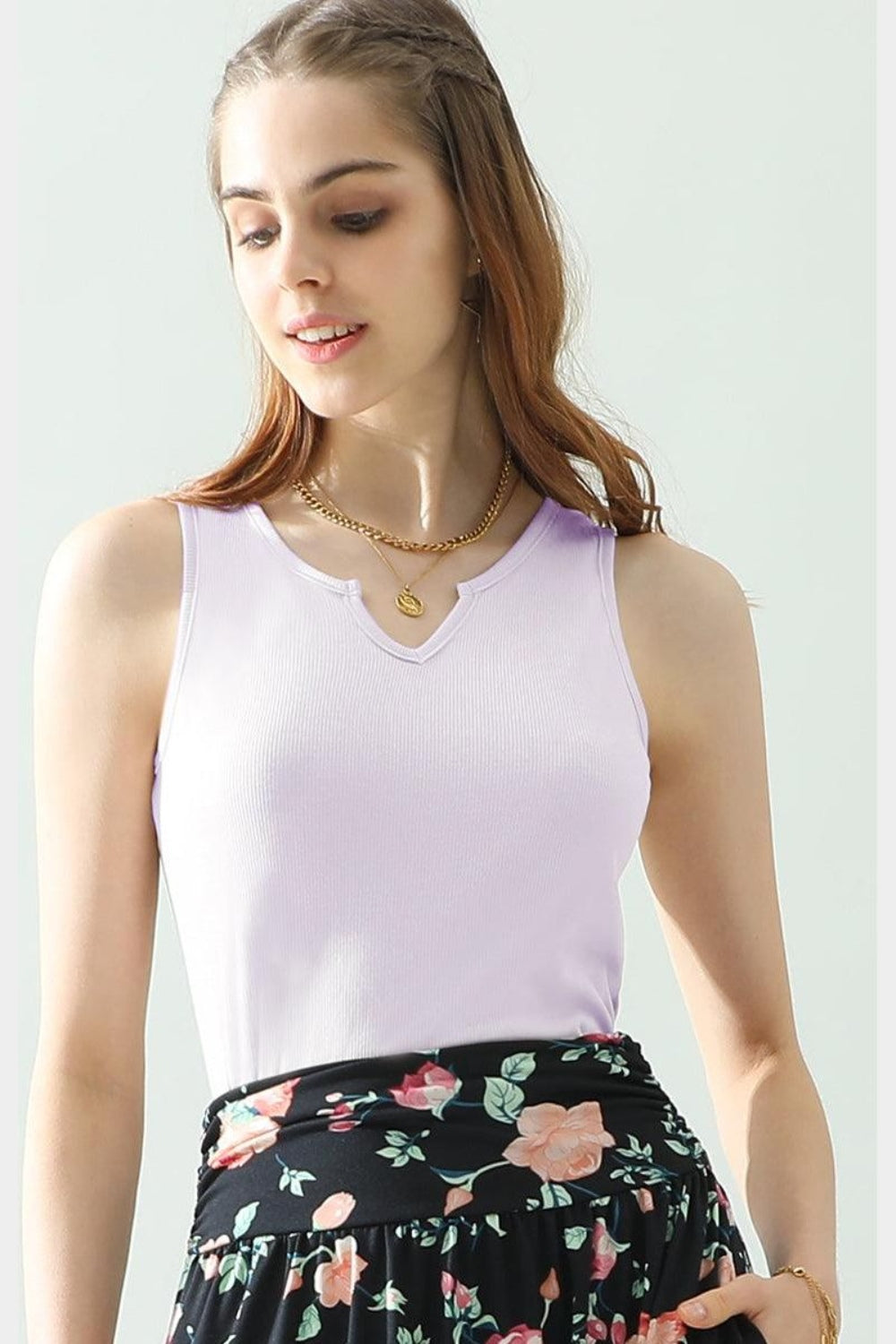 A woman wearing the Ninexis Notched Rib Knit Tank in white paired with a floral skirt and accessorized with a necklace, standing against a light background. This chic look is perfect for any summer wardrobe.