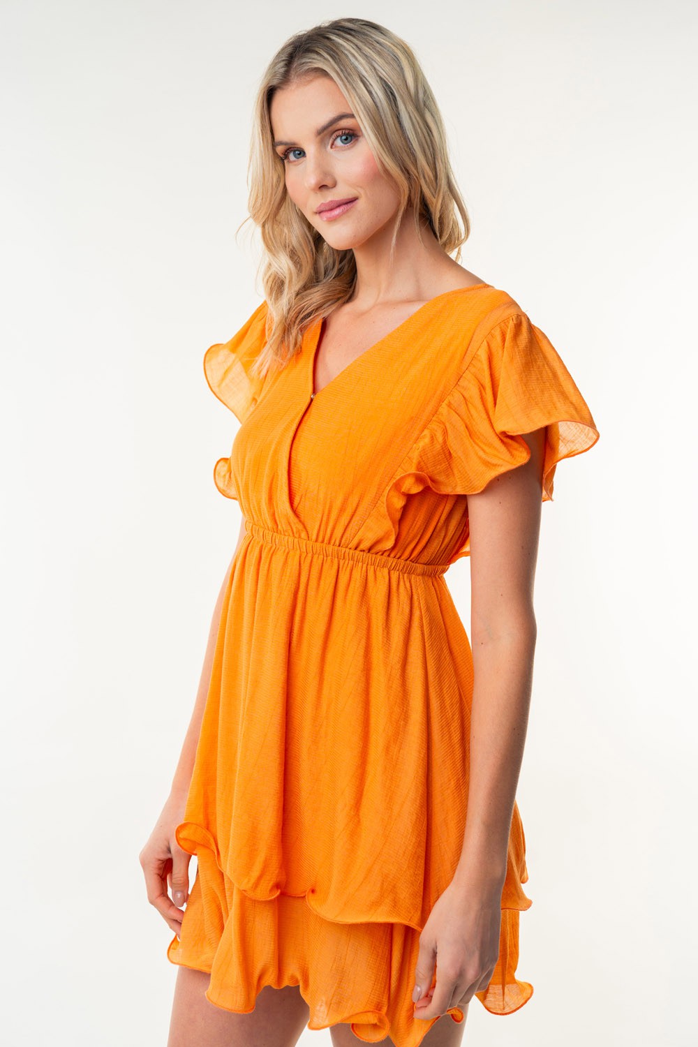 A blonde-haired woman poses against a plain background, wearing the White Birch Full Size Short Sleeve Woven Layered Dress that features ruffled sleeves, a tiered skirt, and an elastic waist.