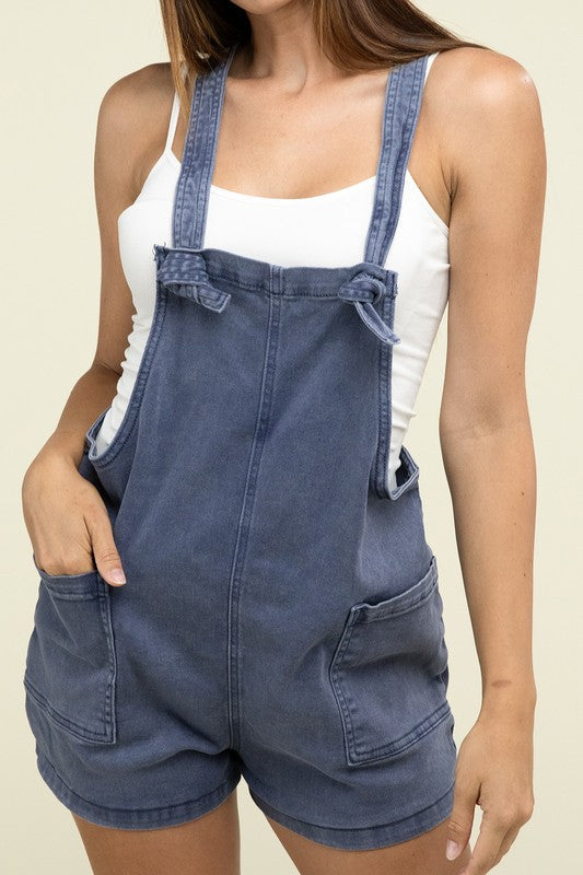 A person wearing the Washed Knot Strap Romper and a white tank top stands against a plain background.