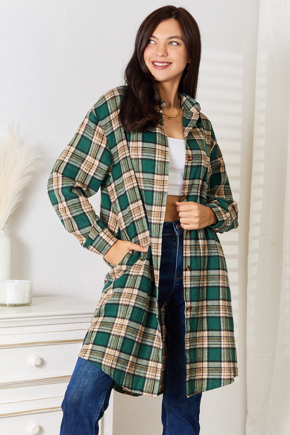 A person wearing the Mandy Plaid Collared Neck Long Sleeve Shirt in green and beige over a white crop top and blue jeans, standing indoors near a white dresser with vases.