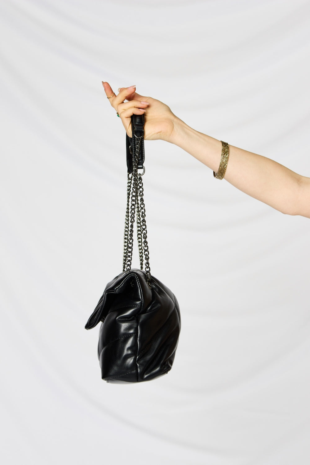 A person holding a stylish SHOMICO PU Leather Chain Handbag over their shoulder against a white background. They are dressed in a beige outfit and looking at the camera, embodying sustainable fashion.