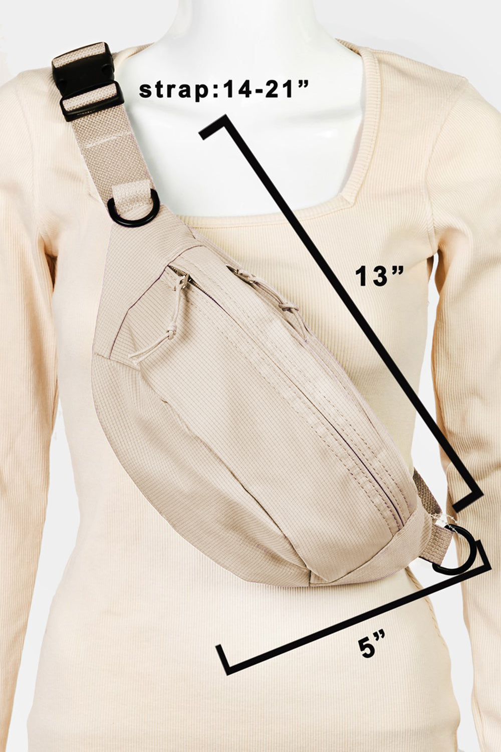 A woman in a black sleeveless top and beige pants stands against a light background, showcasing her versatile accessory—the Fame Adjustable Strap Sling Bag, crafted from durable materials.