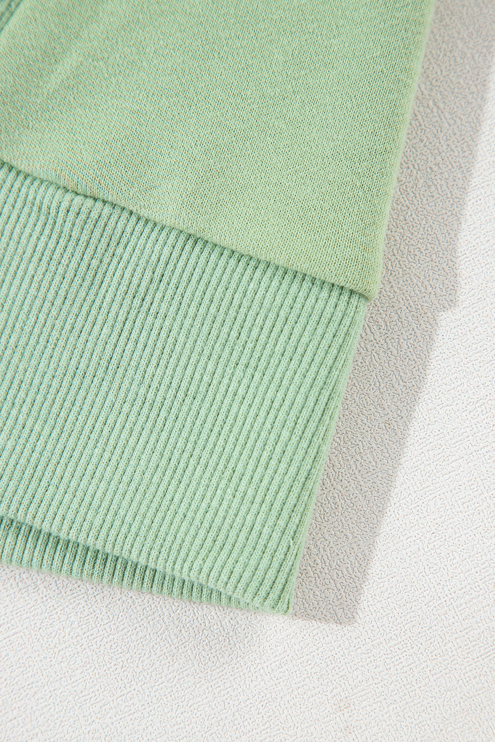 A person with long hair, seen from the back, wearing a Grass Green Solid Fleece Lined Drop Shoulder High Low Sweatshirt and black pants.