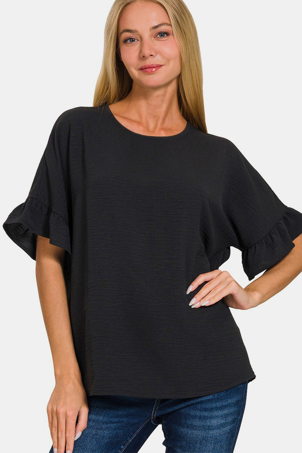 A woman with long blonde hair wears a versatile wardrobe addition: the Zenana V-Neck Flutter Sleeve Top in black paired with blue jeans, posing with one hand on her hip against a plain background.