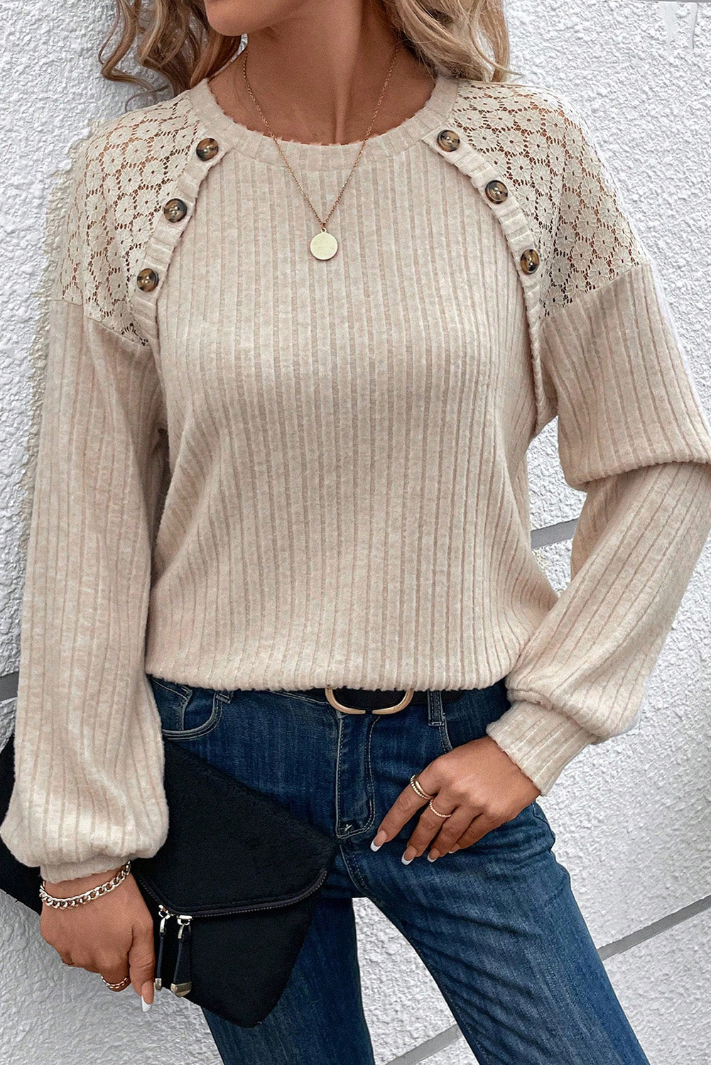 A woman dressed in the Parchment Contrast Lace Raglan Sleeve Buttoned Ribbed Top paired with blue jeans, a pendant necklace, and bracelets. She is holding a black clutch bag and has a hand on her waist.