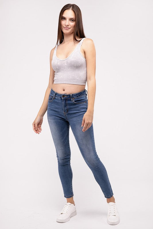 A woman in a Washed Ribbed Cropped V-Neck Tank Top and jeans posing with her hand on her head against a plain background.