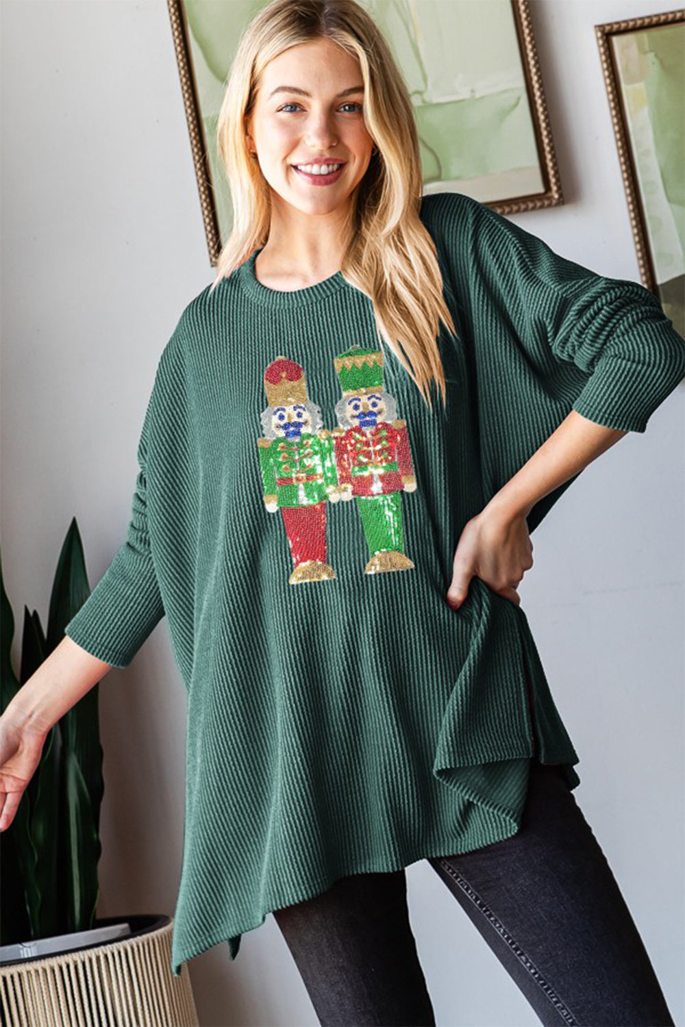 A woman wearing the Heimish Sequin Nutcracker Long Sleeve Ribbed Top smiles while posing indoors, showcasing one of the season's charming holiday outfits.