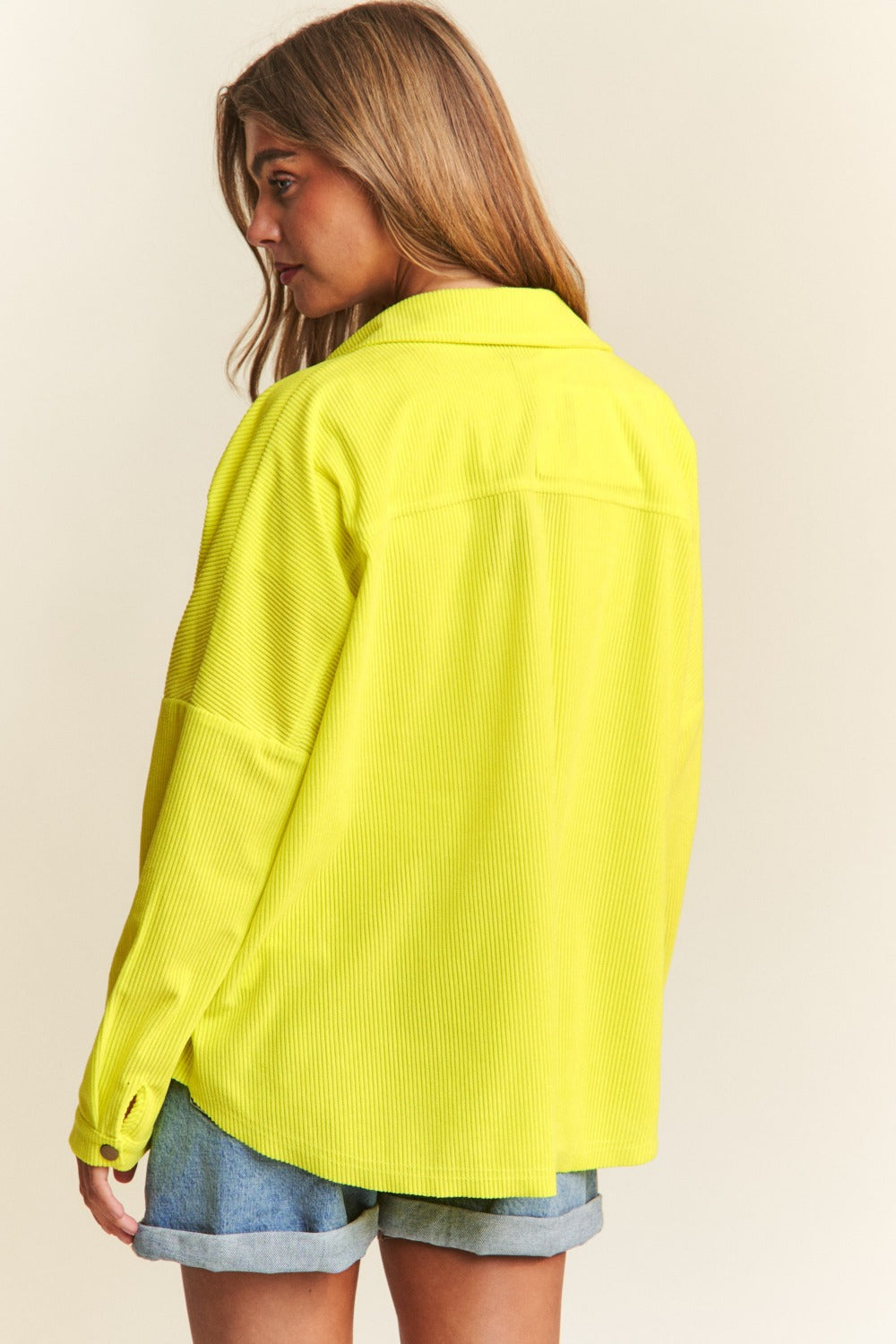 Person wearing a relaxed fit, bright yellow J.NNA Snap Down Long Sleeve High Low Shacket over a white top and denim jeans, smiling against a neutral background.