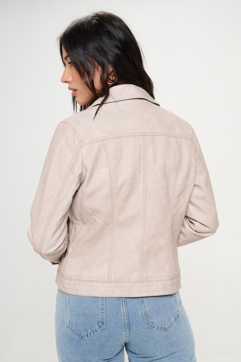 A woman with long dark hair, showcasing women's spring fashion, wears the Coalition LA Button Down Cargo Vegan Leather Shacket over a beige top and blue jeans as she stands against a plain background.