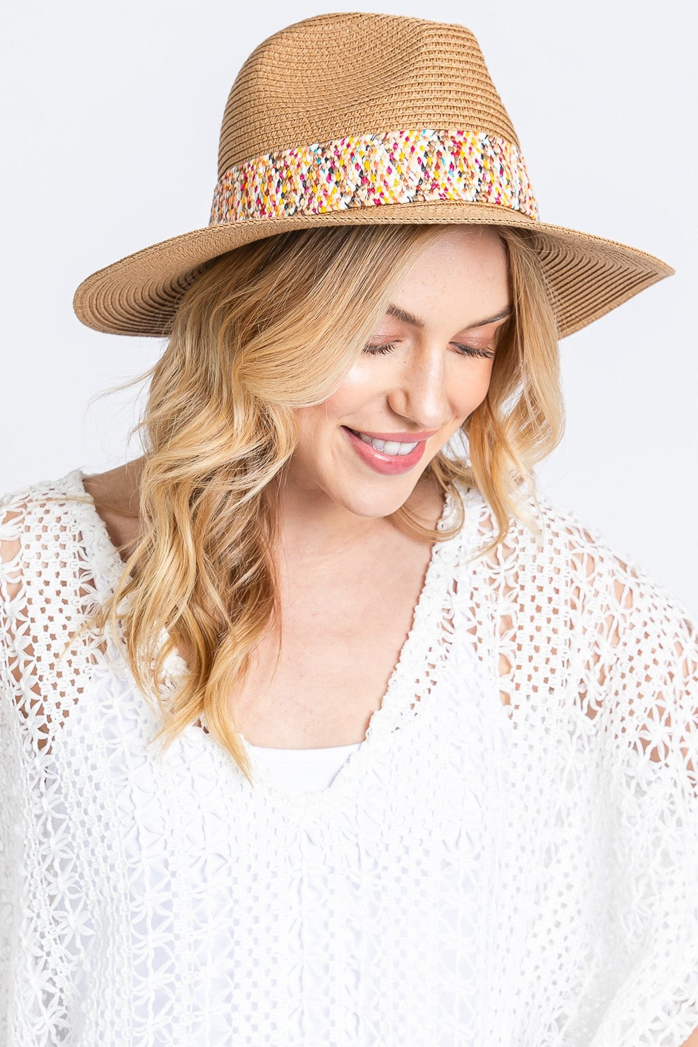 A woman in a chic summer outfit wears the Fame Contrast Detail Wide Brim Straw Hat, featuring a multicolored band. The contrast detail of her white crocheted top enhances her sophistication as she gazes down contemplatively.