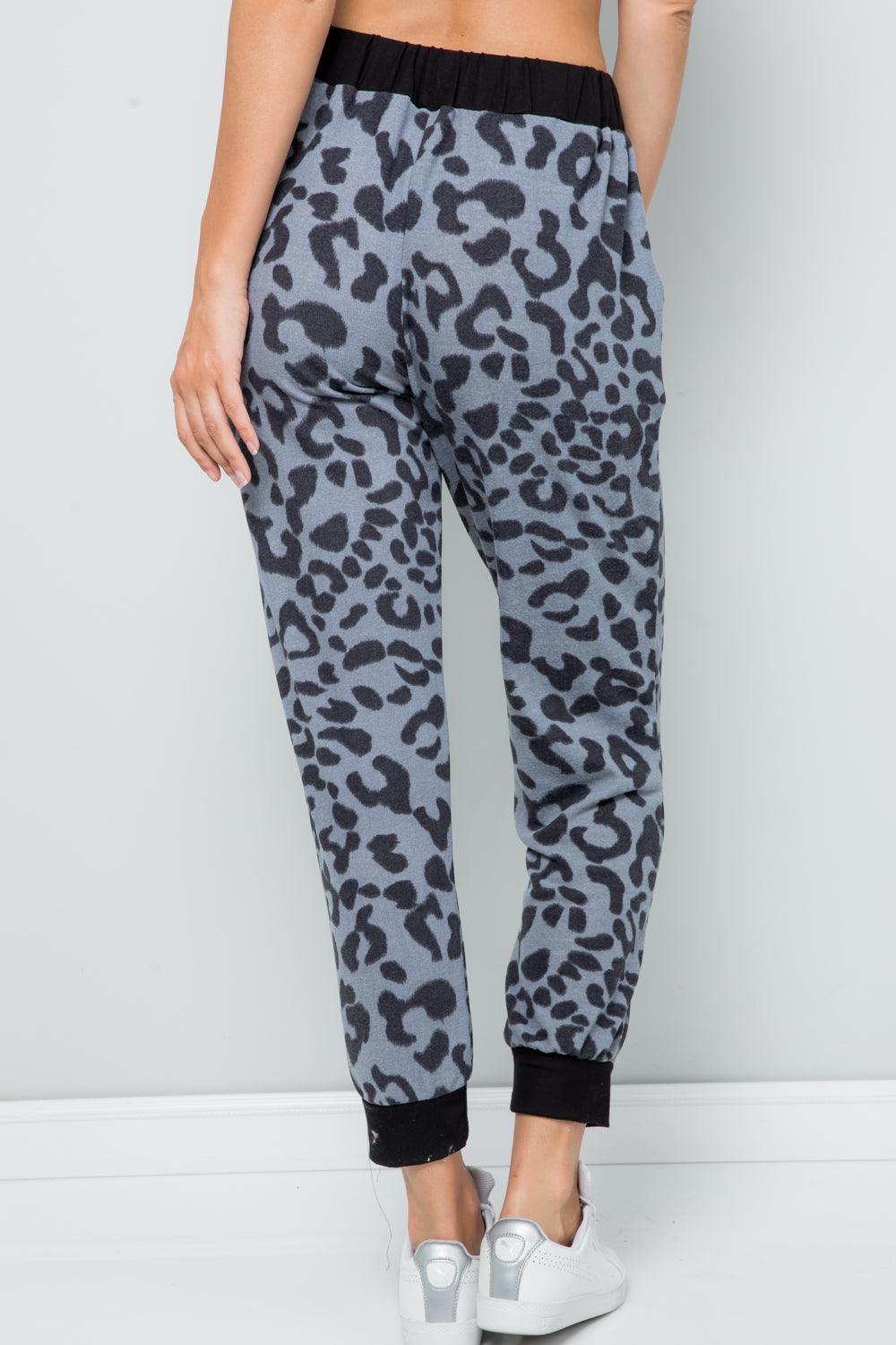 Person wearing Celeste Full Size Leopard Contrast Sweatpants with a black waistband and cuffs, paired with white sneakers, against a plain light gray background.