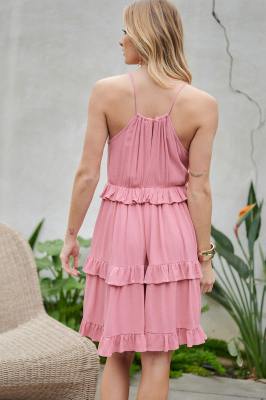 Wearing the Solid Ruffle Sleeveless Mini Dress in blue, the individual near the plants and wicker chair exudes elegance, making it an ideal choice for a casual brunch ensemble.