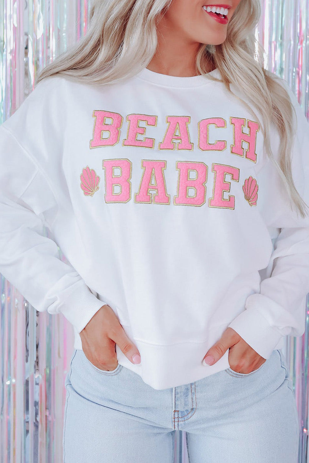 A person with long blonde hair is standing with their back to the camera, wearing a White BEACH BABE Slogan Graphic Casual Sweatshirt and light blue jeans.