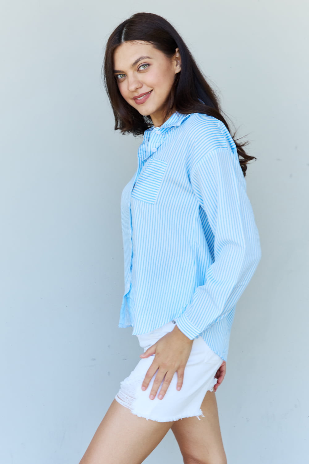 A person with long dark hair smiles while wearing the Doublju She Means Business Striped Button Down Shirt Top in light blue and white shorts, standing against a plain light background.