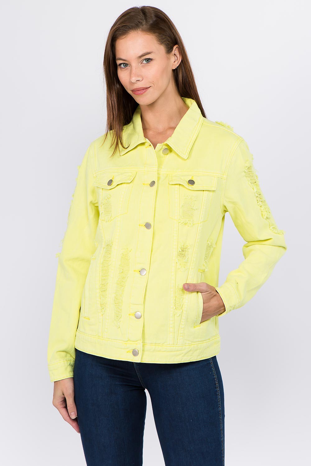 A woman is standing and wearing an American Bazi Distressed Back Button Down Denim Jacket in a vibrant yellow color, complete with large buttons and a unique distressed back design. The slim-fitting jacket pairs perfectly with her dark blue jeans as she poses confidently with one hand in her pocket.