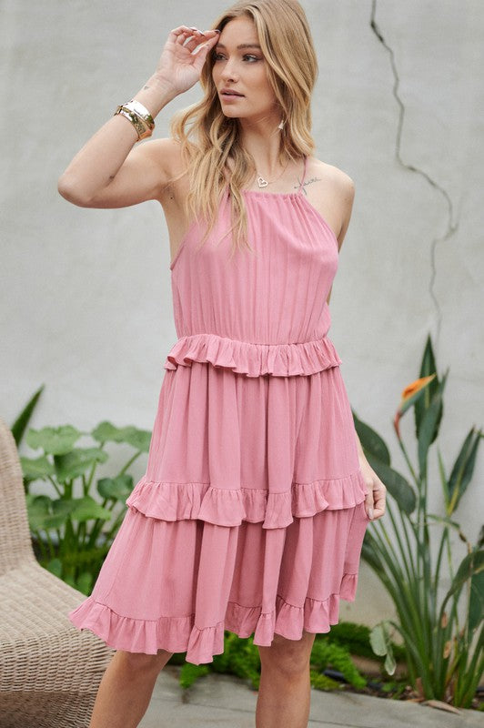 Wearing the Solid Ruffle Sleeveless Mini Dress in blue, the individual near the plants and wicker chair exudes elegance, making it an ideal choice for a casual brunch ensemble.