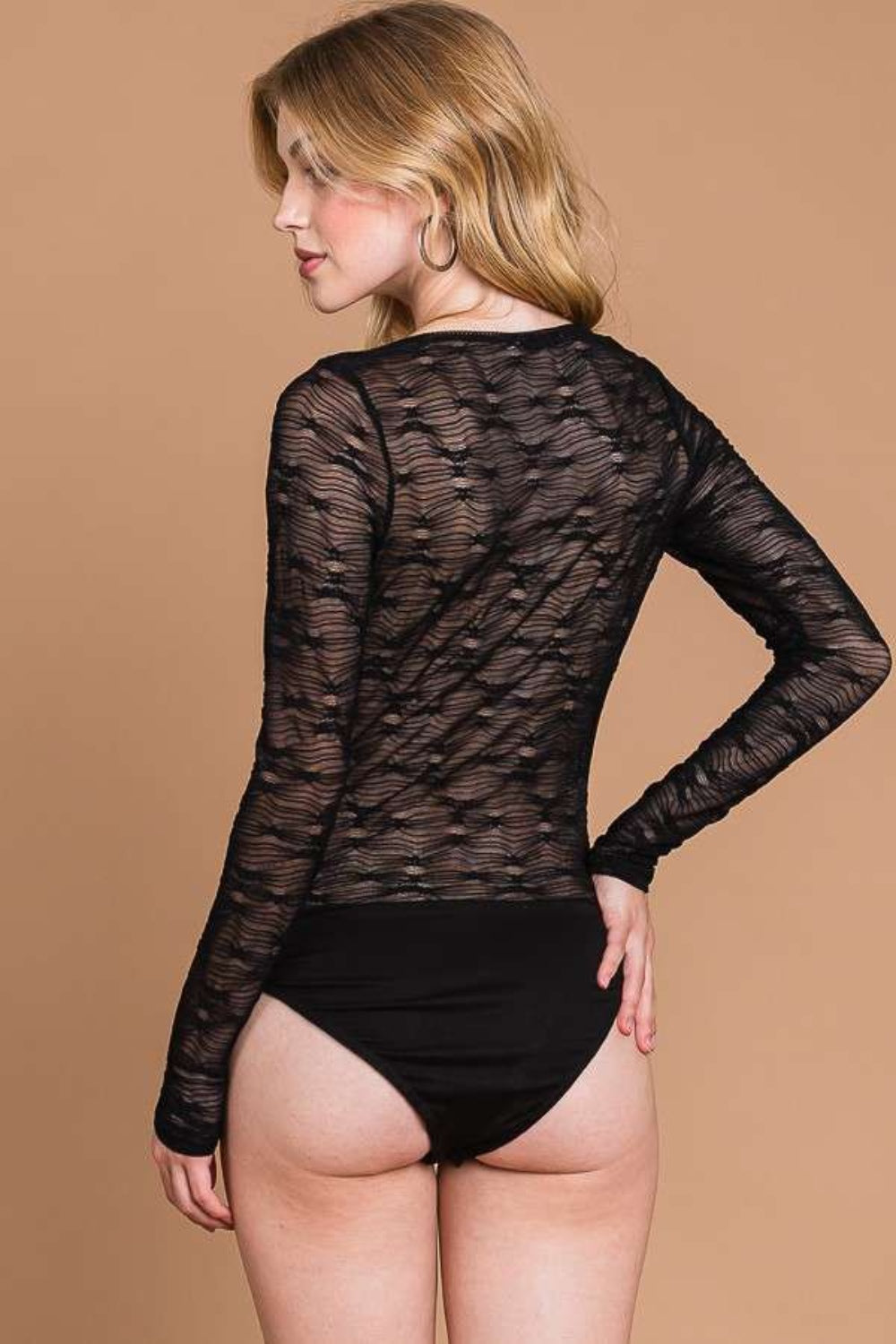 A woman wearing the Culture Code Round Neck Mesh Perspective Bodysuit, paired with black bottoms, stands against a plain brown background.