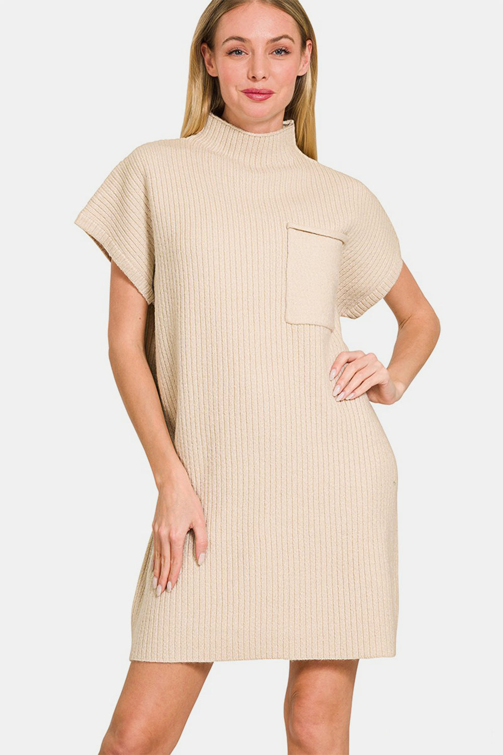 A woman is posing against a white background while wearing the Zenana Short Sleeve Sweater Mini Dress, a beige, ribbed mini dress with short sleeves and a high neck. It features a front pocket and effortlessly combines style and function.