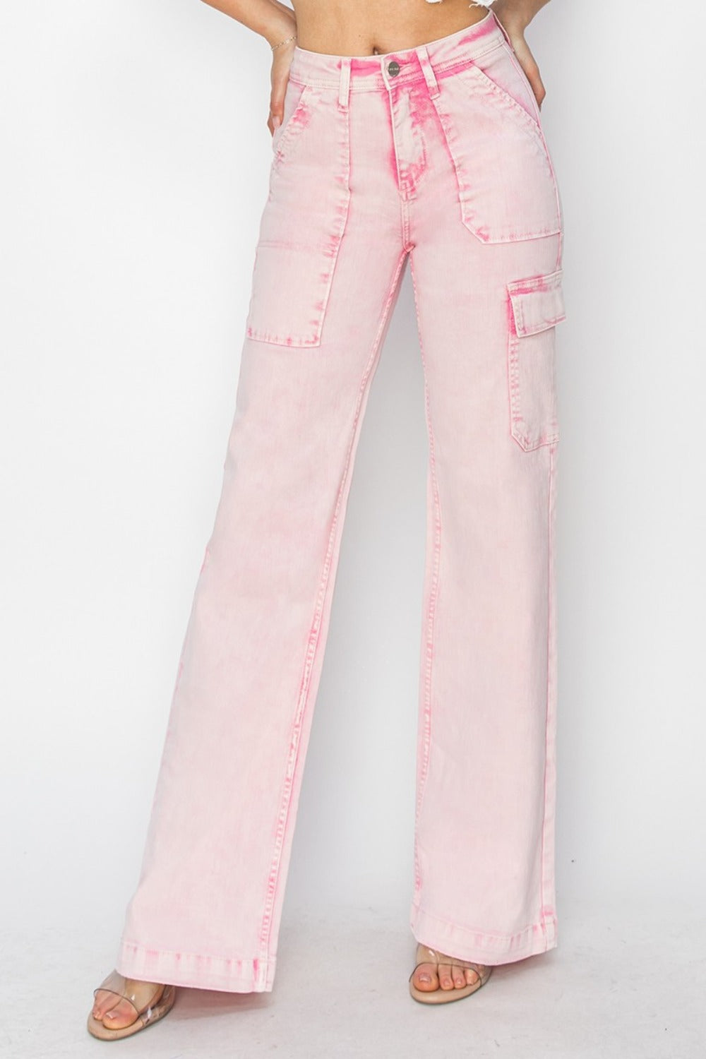 Person wearing the RISEN Full Size High Rise Wide Leg Cargo Pocket Jeans in light pink, featuring front pockets and a button-zip closure, standing against a white background.