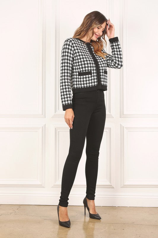 A woman dressed in the Black Check Knitted Jacket, featuring snap buttons and functional pockets, complemented by black pants, stands against a white background.