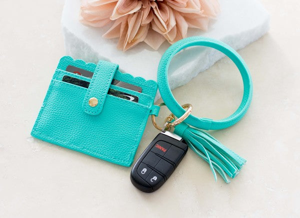 A person's lap with a Key Ring ID Wallet Bracelet featuring button snap closure, car keys on a key ring, and a hand with white nail polish.