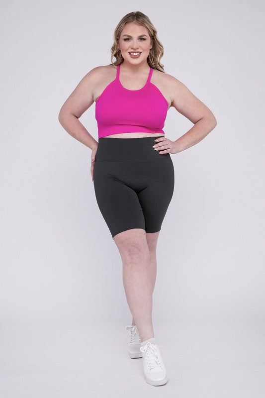 Against a plain background, a person showcases the Plus Athletic High Rise Biker Shorts in coral, crafted from high-quality athletic fabric and paired with a pink top.