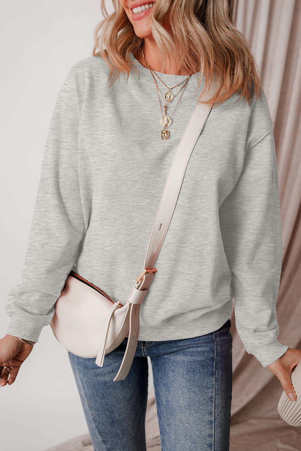 A woman with wavy hair is seen from behind wearing a Gray Solid Fleece Lined Drop Shoulder Terry Sweatshirt, blue jeans, and carrying a light-colored shoulder bag with a matching clutch.