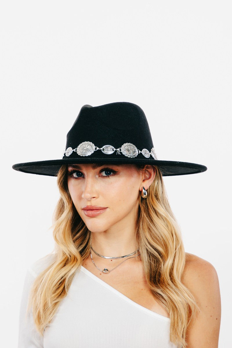 Wearing the Fame Metal Trim Flat Brim Fedora Hat with decorative accents, paired with a single-shoulder white top and layered necklaces, this person showcases the perfect blend of style and fashion accessory.