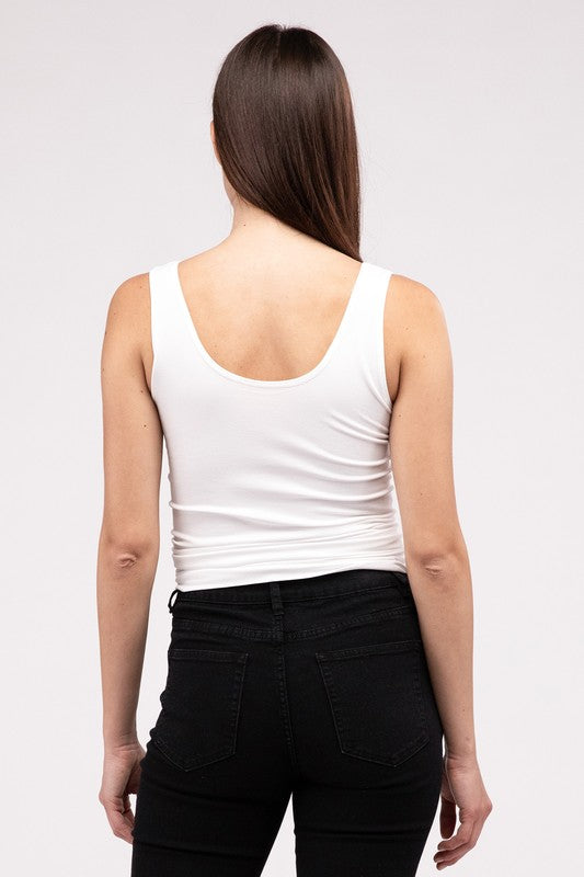 A woman in a white Front & Back 2-Way V-Neck Seamless Tank and black pants, standing with hands on hips and looking at the camera.