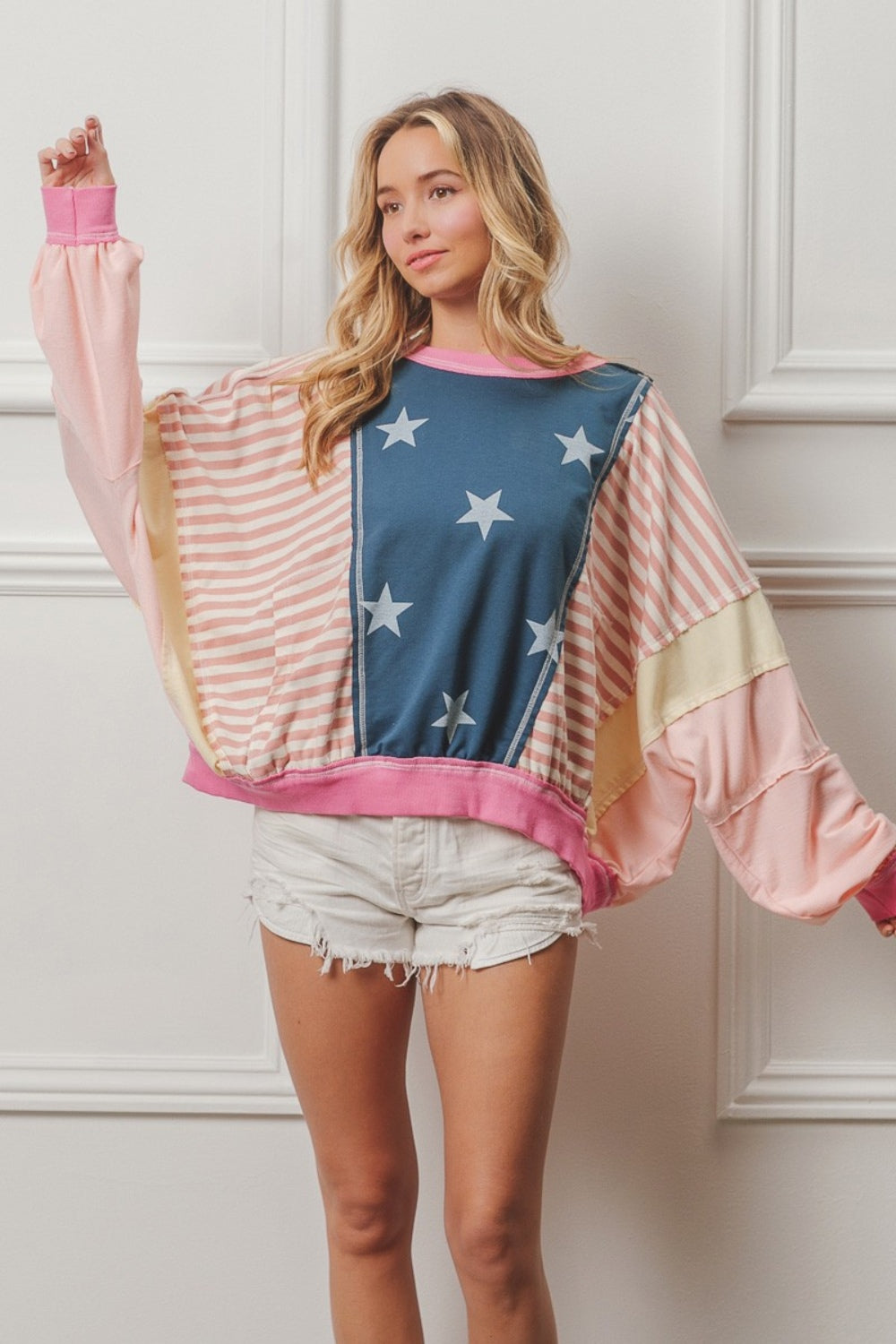 A woman wearing a BiBi Stars and Stripes Round Neck Long Sleeve Top paired with white shorts, standing against a plain background.