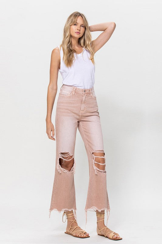 Person wearing 90's Vintage Crop Flare Jeans in rose pink with high waist, distressed details, rips on the knees, and frayed hems, paired with beige strappy sandals.