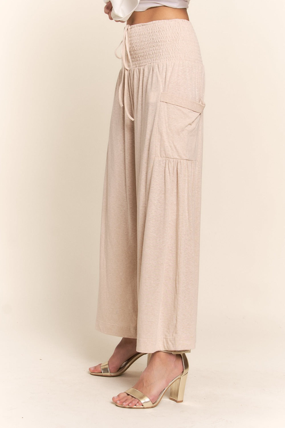 A person wearing J.NNA Smocked Waist Boho Wide Leg Pants with Pockets in beige stands in low-heeled sandals against a plain background, paired with a chic white T-shirt.