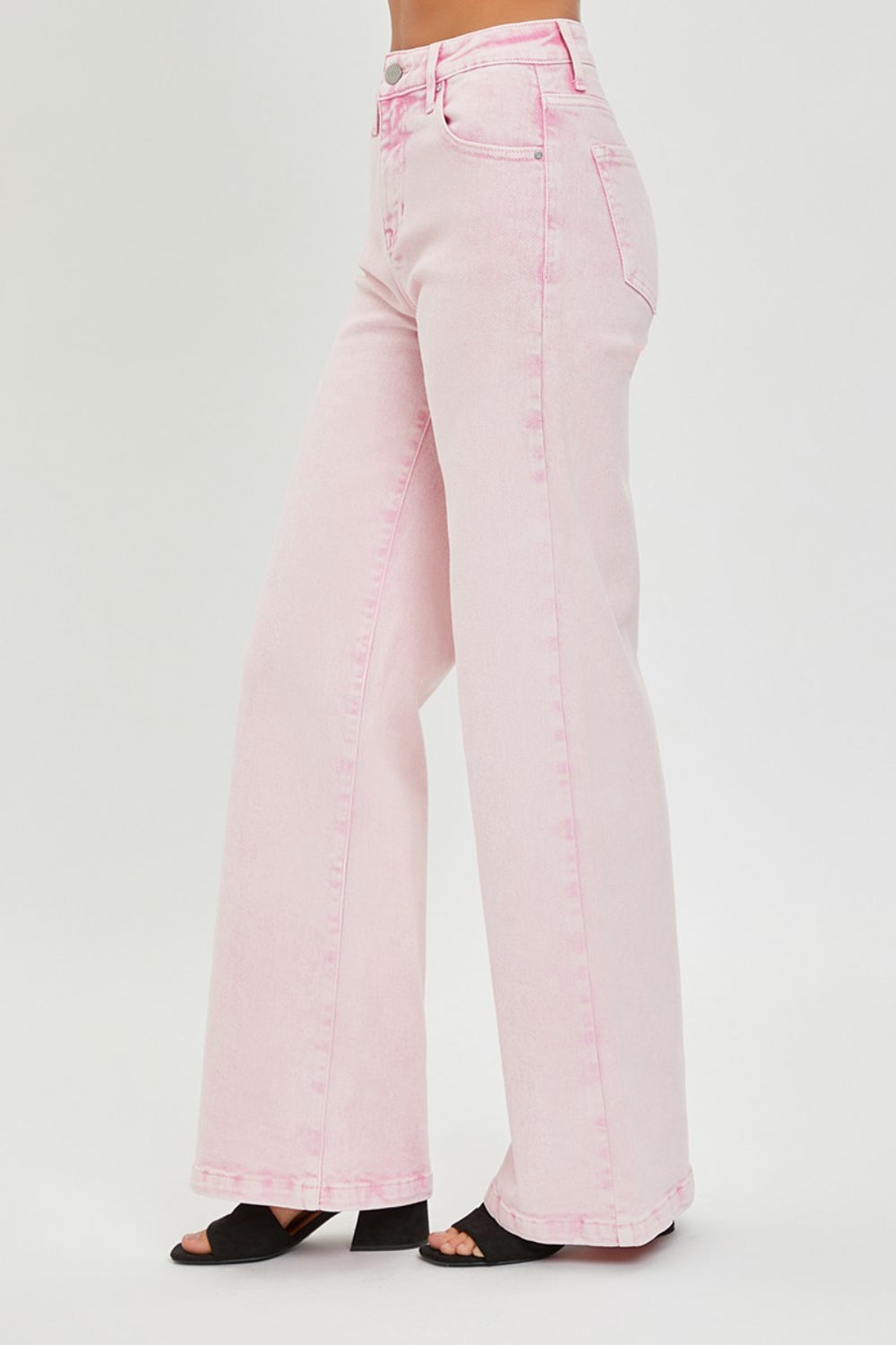 Someone is wearing RISEN Full Size High Rise Tummy Control Wide Leg Jeans in light pink, paired with black heeled sandals against a plain white background.