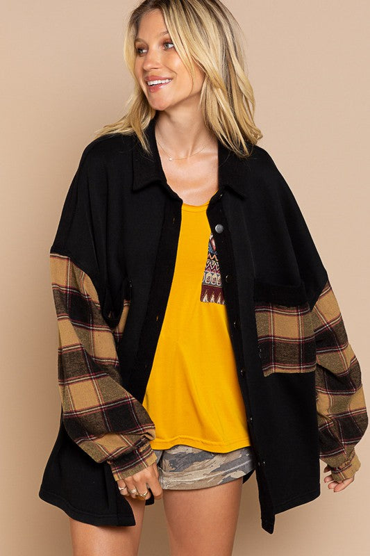 A person wearing the Long Sleeve With Plaid Detail Sleeve Shacket in brown, featuring plaid details on the sleeves and a matching pocket, paired with a white top underneath and a wide-brimmed hat—perfect for transitional weather.